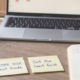 Calm wooden desk with three yellow sticky notes reading "Win = data, not proof", "Same size next trade" and "Set the limit first", beside a notebook, blue Bic pen, coffee and a laptop showing a candlestick chart.