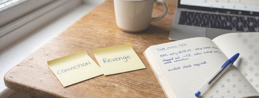 Two yellow sticky notes on a warm wooden desk labelled CONVICTION and REVENGE, beside an open trading journal with handwritten notes and a blue Bic pen, laptop with candlestick chart in background, natural daylight.