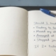 A flat-bound notebook open on a wooden desk with a handwritten pre-session check headed 'Should I trade today?', four warning-sign questions, and 'flat day' circled, a blue Bic pen on the page.