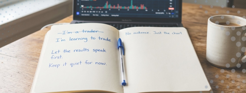 A trading journal reading I'm learning to trade beside a laptop chart on a wooden desk