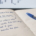 Open notebook on a wooden desk with handwritten notes in blue ink: "Daily target: make X a day" crossed out, then "It's not about the money" and a list starting with a circled "1 trade".
