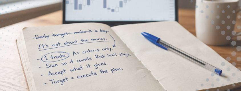 Open notebook on a wooden desk with handwritten notes in blue ink: "Daily target: make X a day" crossed out, then "It's not about the money" and a list starting with a circled "1 trade".